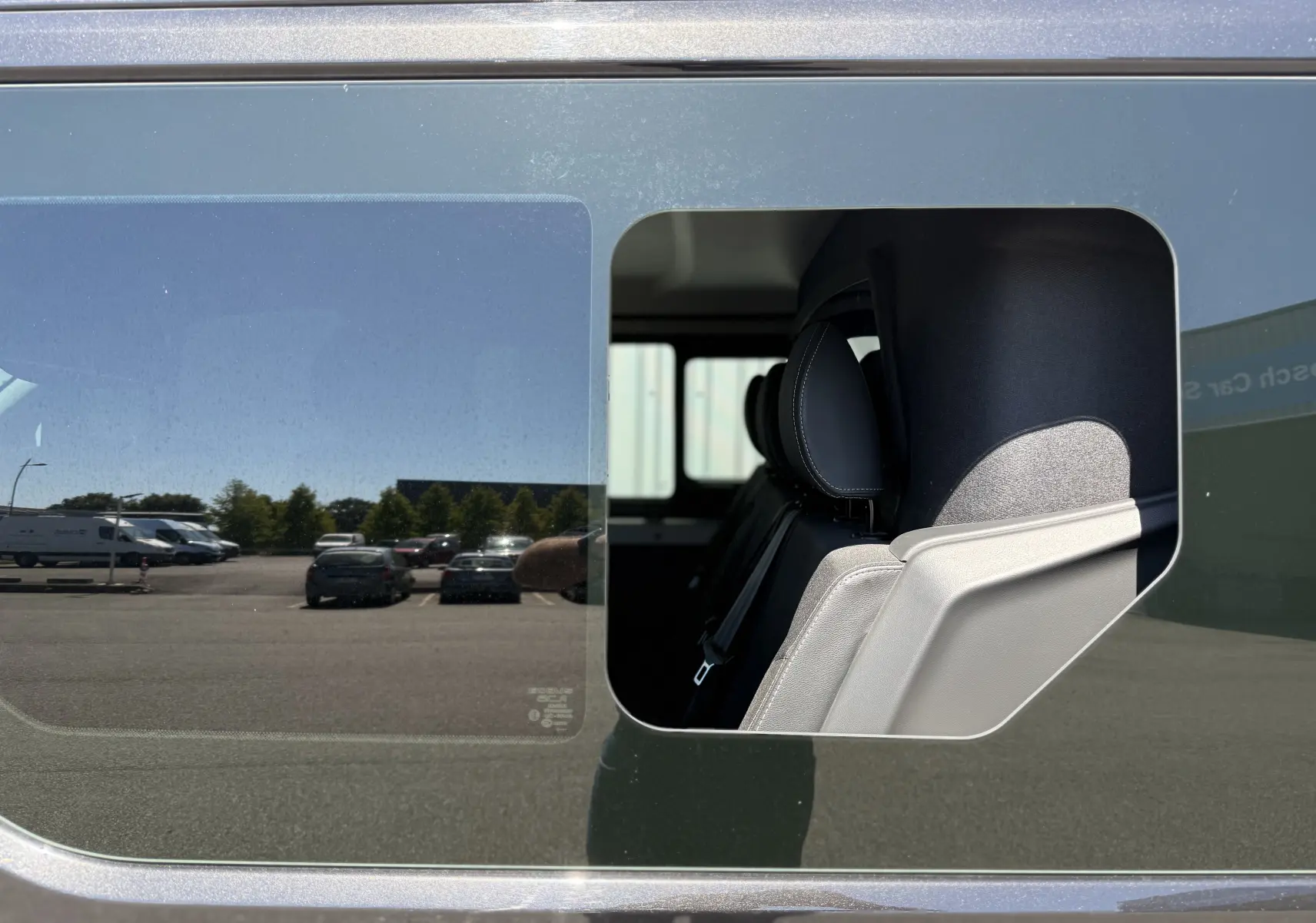 Vue latérale du Renault Trafic gris montrant une fenêtre latérale ouverte avec sièges arrière en tissu visibles.