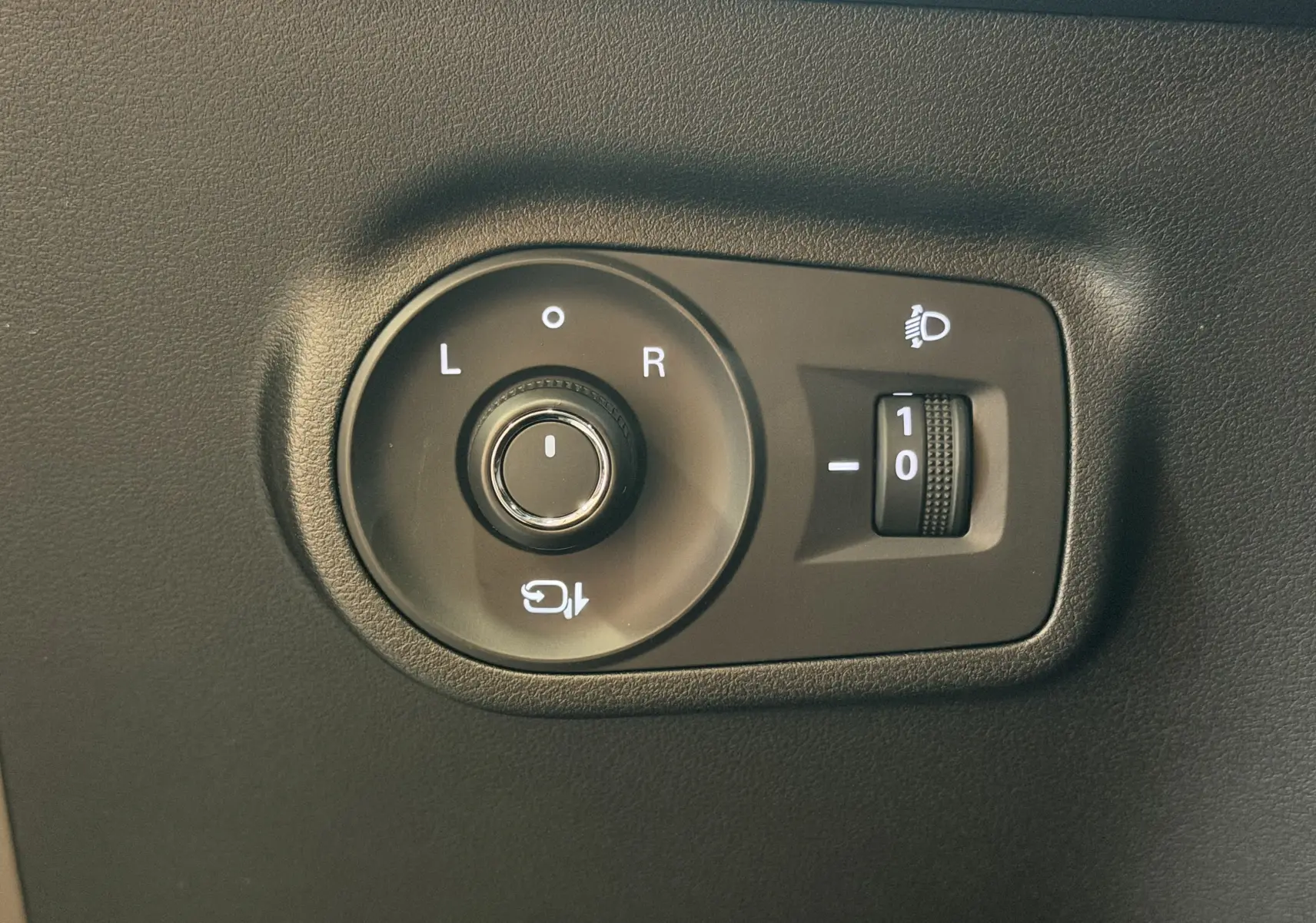 Gros plan sur la commande de réglage des rétroviseurs et des phares du MG MOTOR ZS 2026 en intérieur noir.