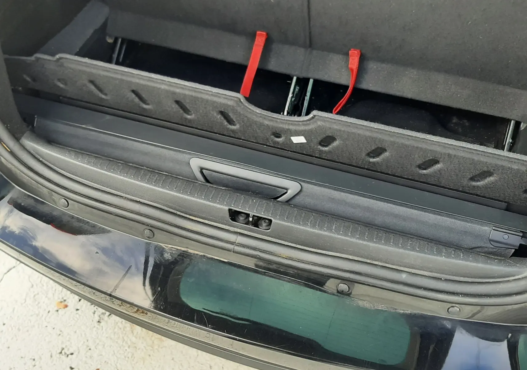 Vue plongeante sur le coffre arrière ouvert d'un Renault Grand Scenic noir, montrant les sangles rouges des sièges rabattables.