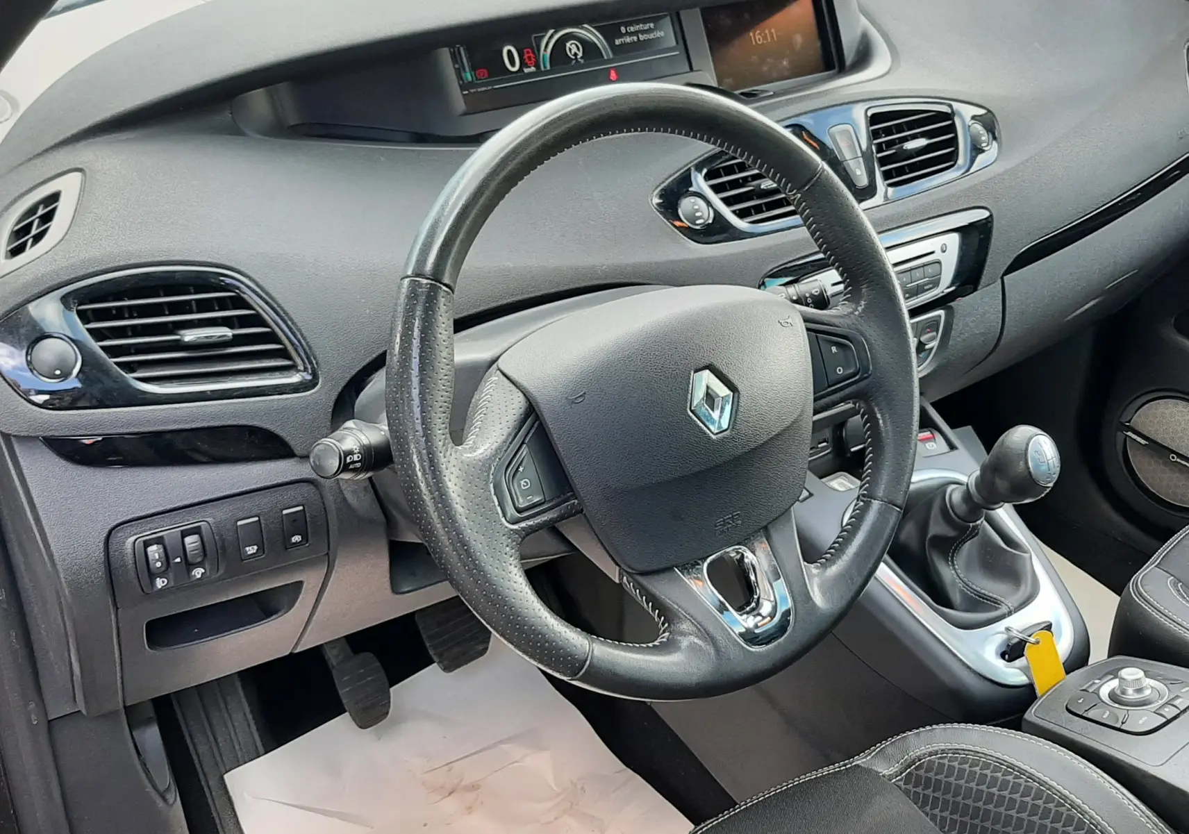 Vue intérieure du poste de conduite du Renault Grand Scenic noir, avec volant cuir, tableau de bord digital et levier de vitesse manuel.