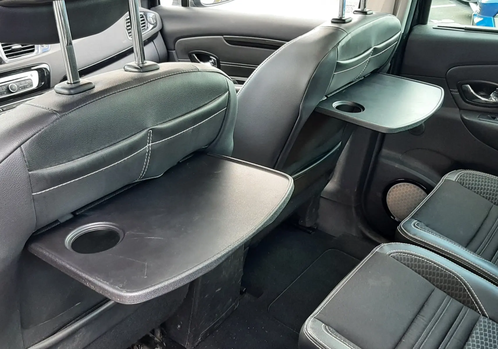 Vue intérieure arrière droite du Renault Grand Scenic noir 7 places, avec tablettes rabattables sur les dossiers des sièges avant.