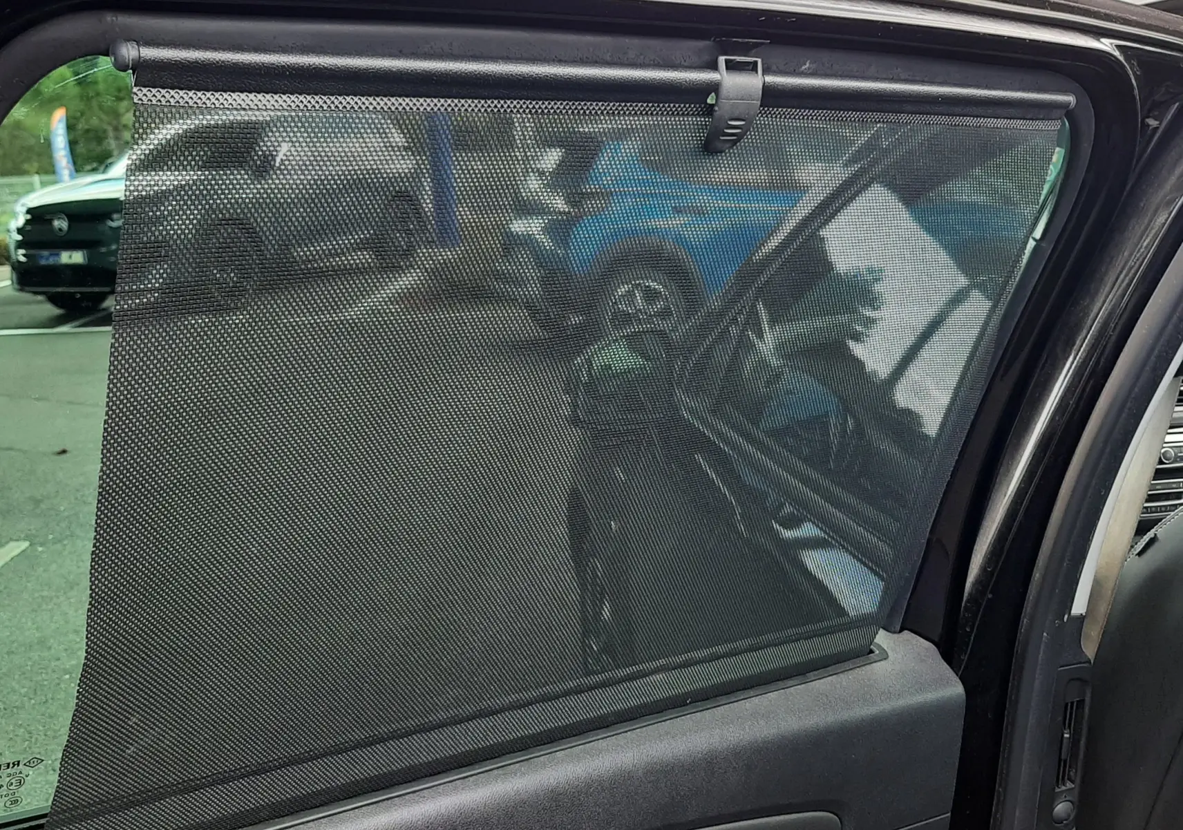 Vue intérieure côté gauche de la porte arrière d'un Renault Grand Scenic noir avec store pare-soleil déployé.