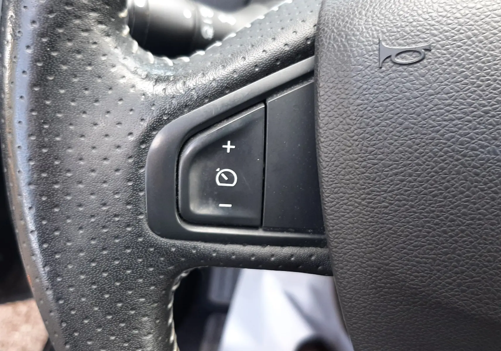 Gros plan sur le volant en cuir noir perforé du Renault Grand Scenic DCI 110 Bose, avec commandes de régulateur de vitesse.