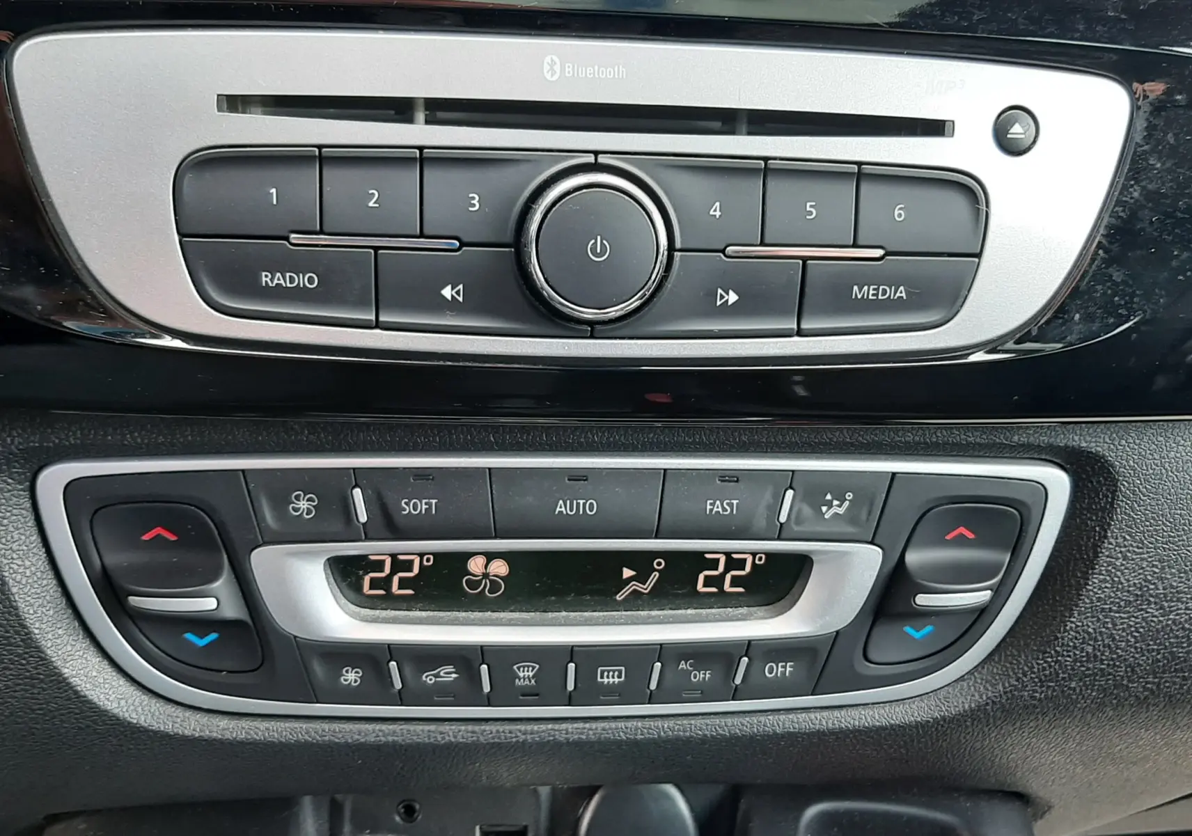Gros plan sur la console centrale noire du Renault Grand Scenic 2015, affichant la radio et la climatisation digitale à 22°C.
