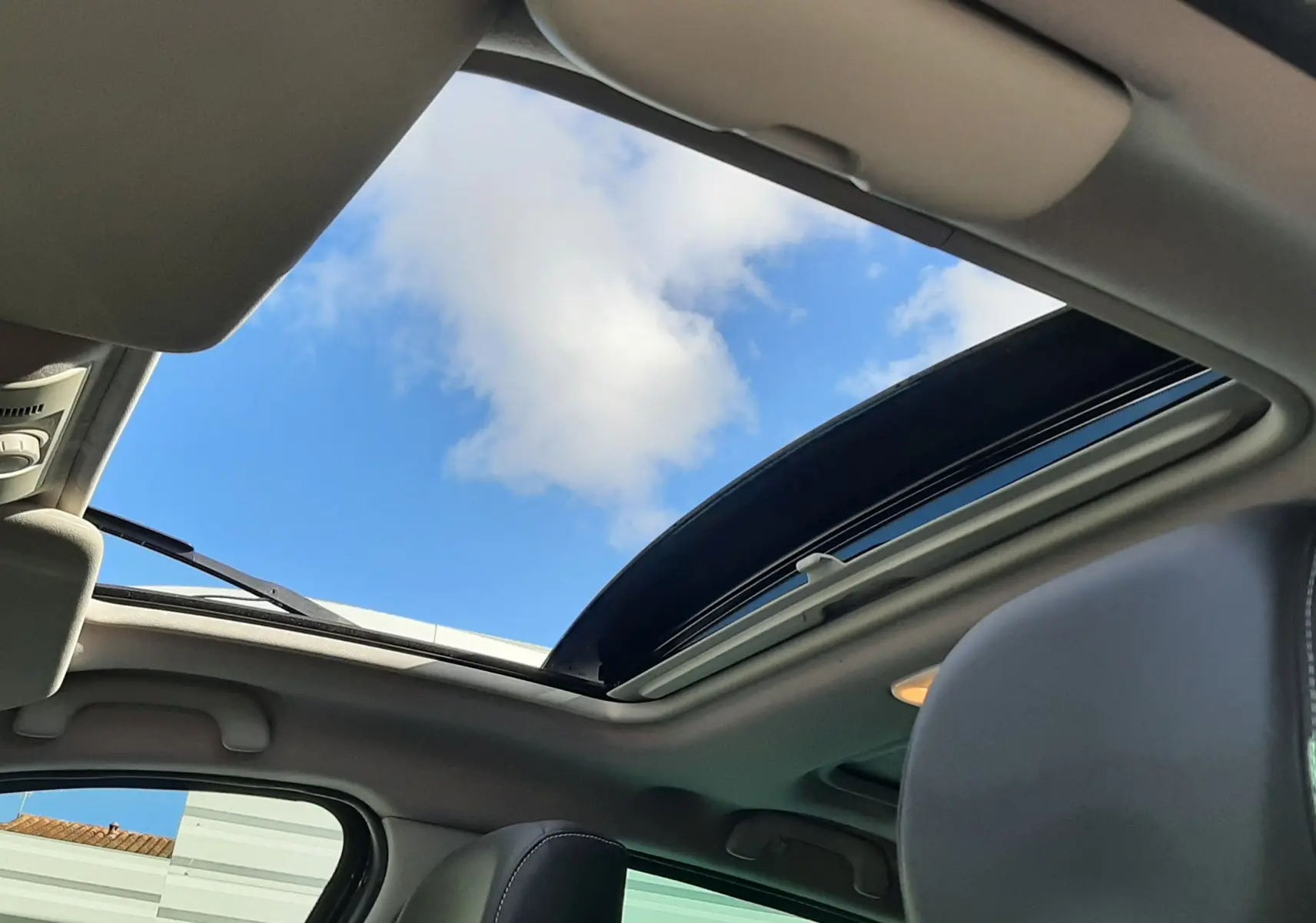Vue intérieure du toit ouvrant panoramique du Renault Grand Scenic noir, avec ciel bleu visible à travers la vitre ouverte.