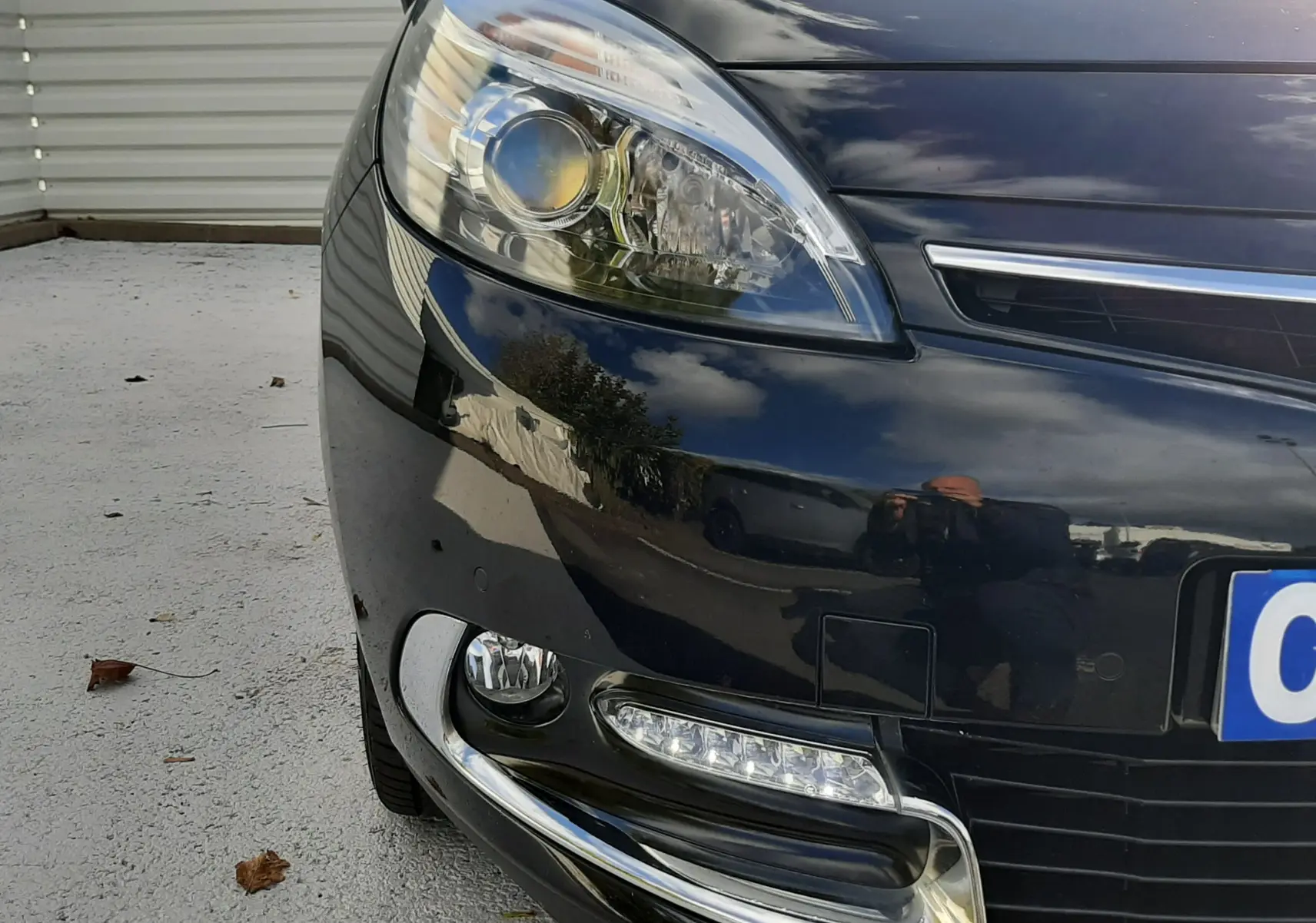 Gros plan sur l'avant gauche noir brillant du Renault Grand Scenic 2015, mettant en valeur le phare et les feux LED.