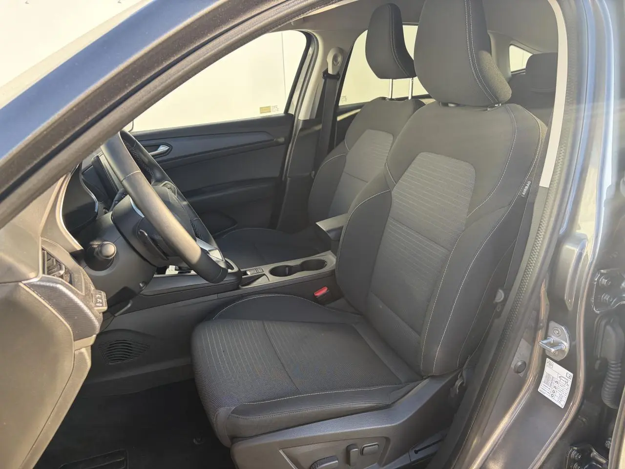 Vue intérieure côté conducteur de la Renault Arkana 2025, sièges noirs avec réglage électrique et accoudoir central.