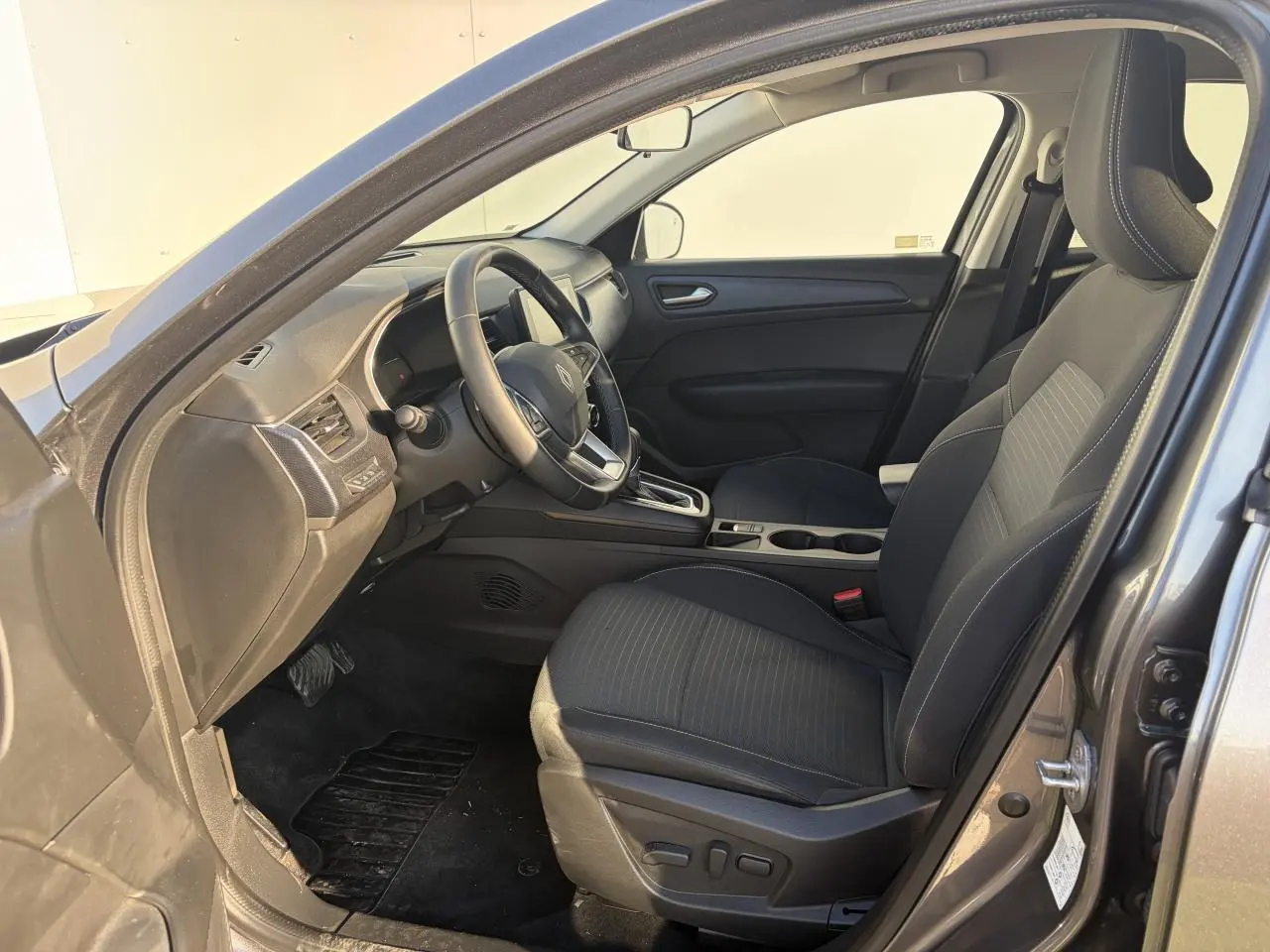 Vue intérieure côté conducteur de la Renault Arkana 2025, sièges noirs avec réglages électriques et volant textile grainé.