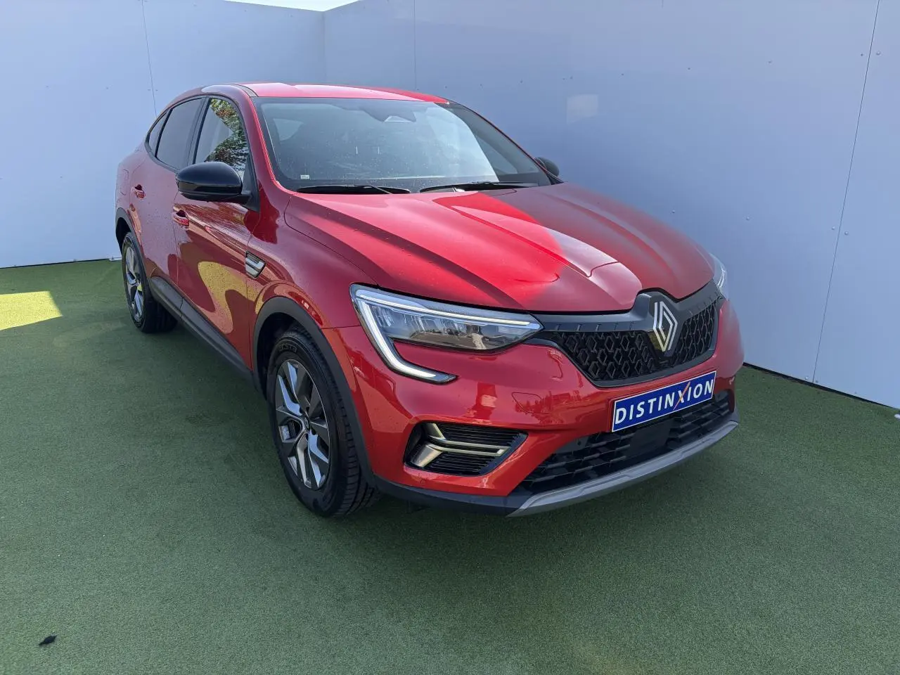 Renault Arkana rouge flamme métal vu en 3/4 avant droit, avec calandre noire et jantes alliage grises 17 pouces.