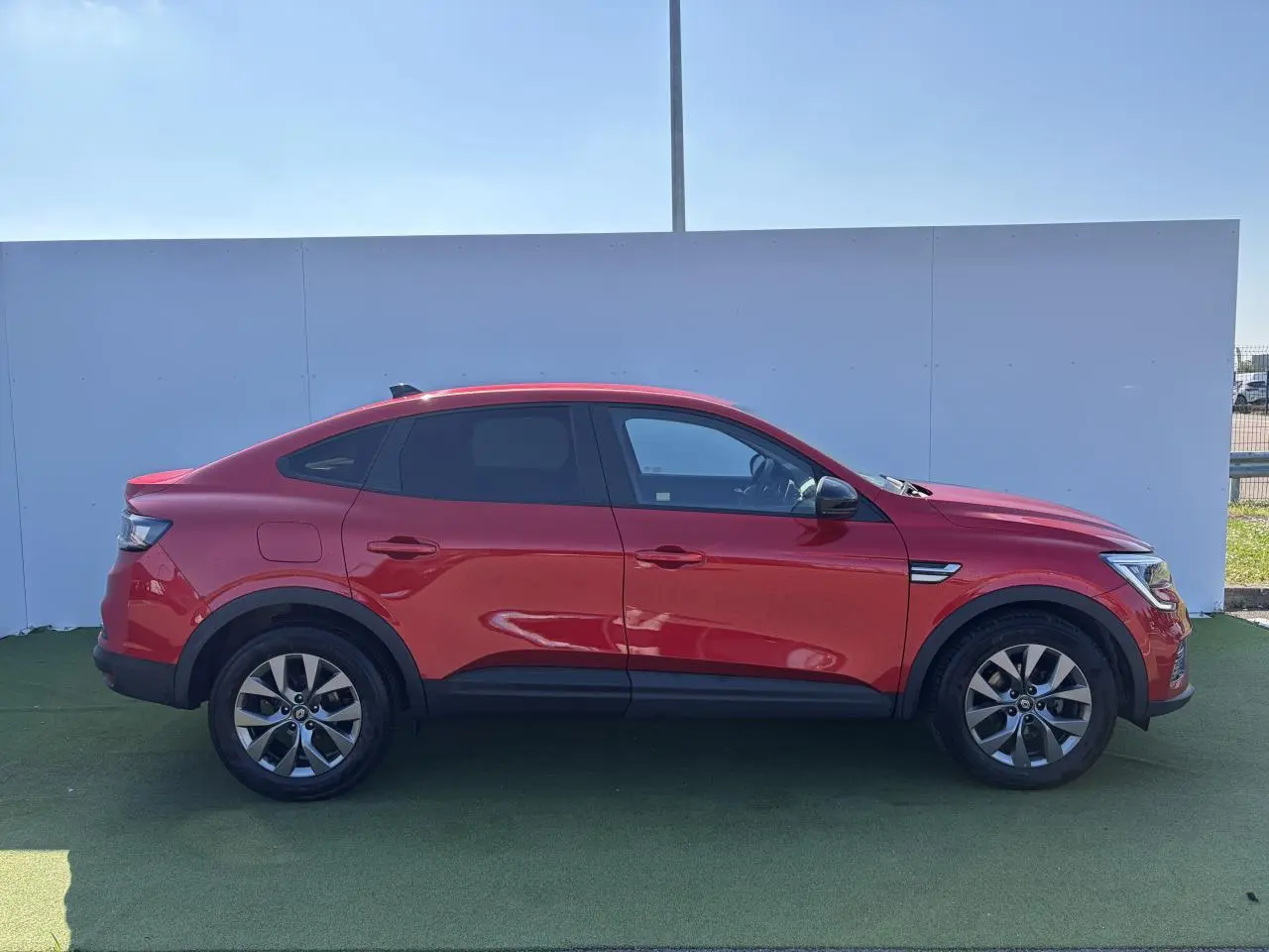 Profil droit d'un Renault Arkana rouge flamme métallisé 2025 avec jantes alliage et vitres surteintées.