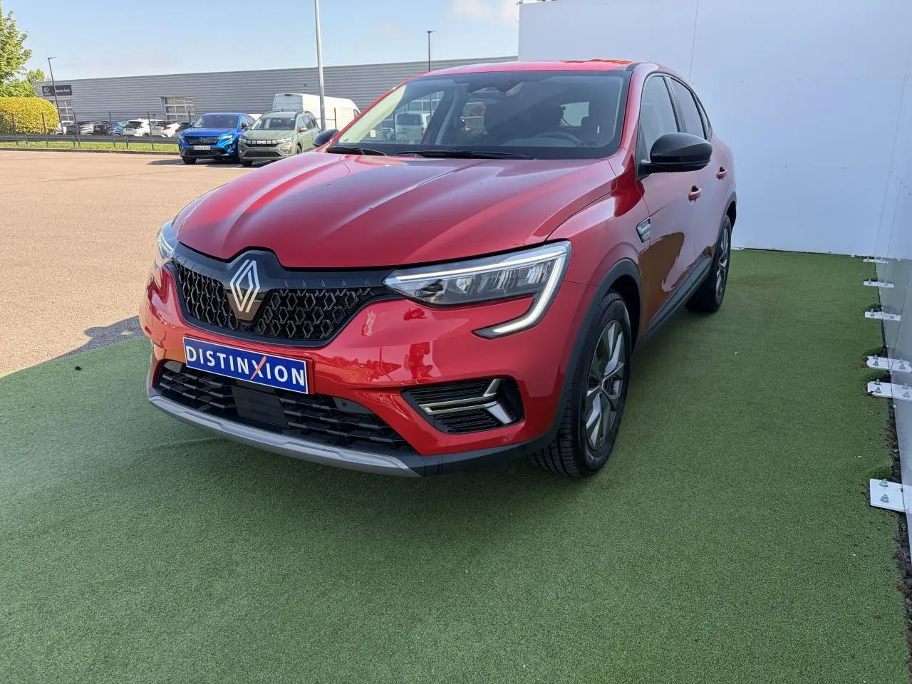 Renault Arkana rouge flamme métal vu en 3/4 avant droit, avec calandre noire et jantes alliage grises 17 pouces.