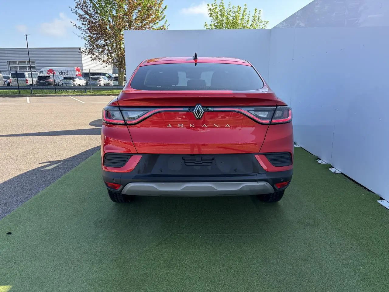 Vue arrière d'une Renault Arkana rouge flamme métal 2025 avec feux LED reliés et lunette arrière surteintée.