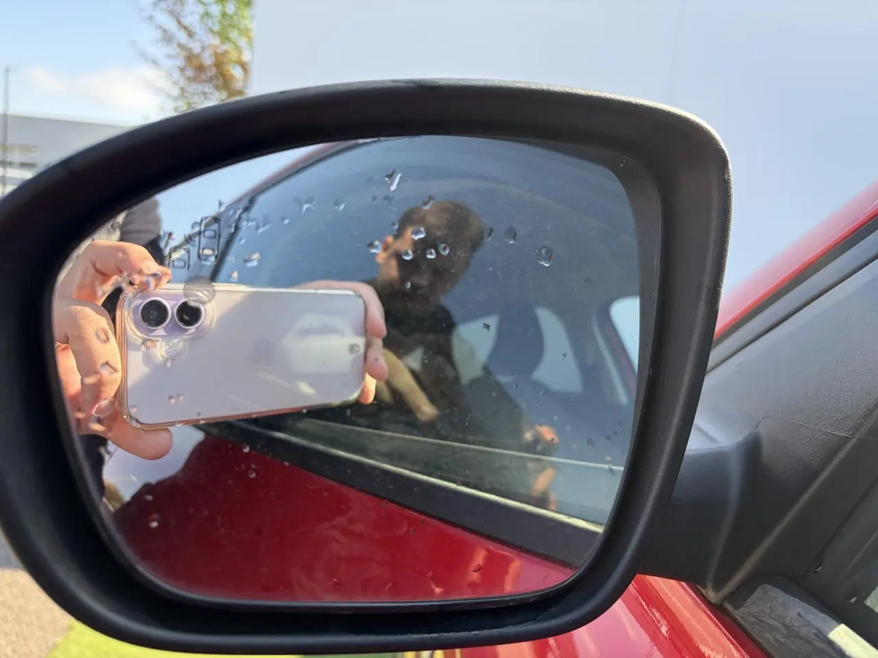 Rétroviseur extérieur côté gauche d’un Renault Arkana rouge flamme métal avec reflet partiel de la portière et d’une personne.