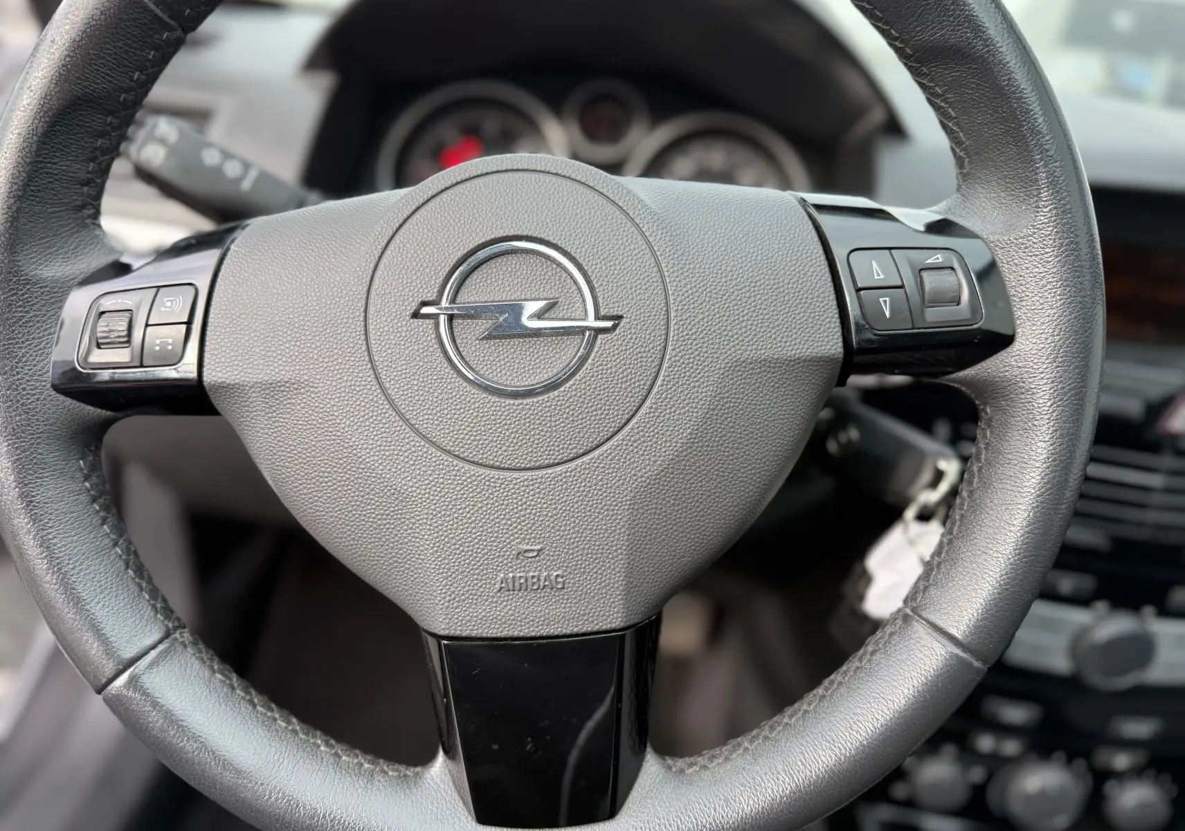 Gros plan sur le volant en cuir noir de l'Opel Astra 1.7 CDTI 110, avec commandes intégrées et logo Opel central.