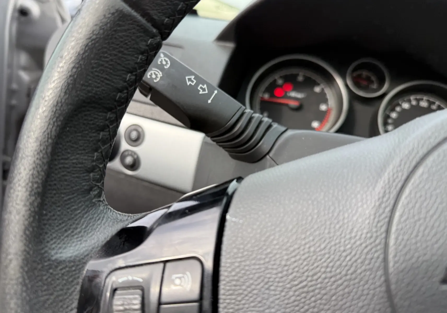 Gros plan sur le volant en cuir noir et la commande de clignotants d'une Opel Astra gris, tableau de bord en arrière-plan flou.