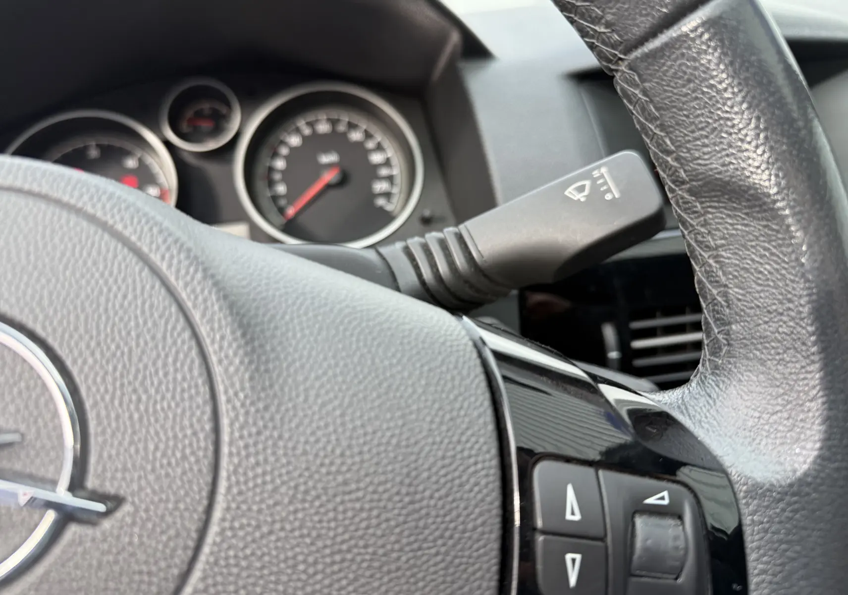 Gros plan sur le volant cuir noir d’une Opel Astra 2010, avec commandes intégrées et tableau de bord en arrière-plan.