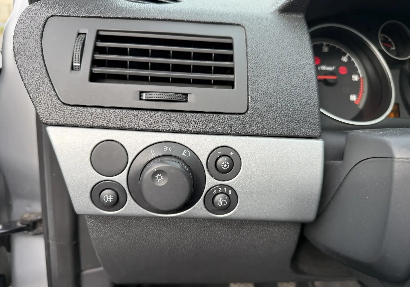 Détail du tableau de bord gris de l'Opel Astra 1.7 CDTI 110 de 2010 avec commandes d'éclairage et ventilation.