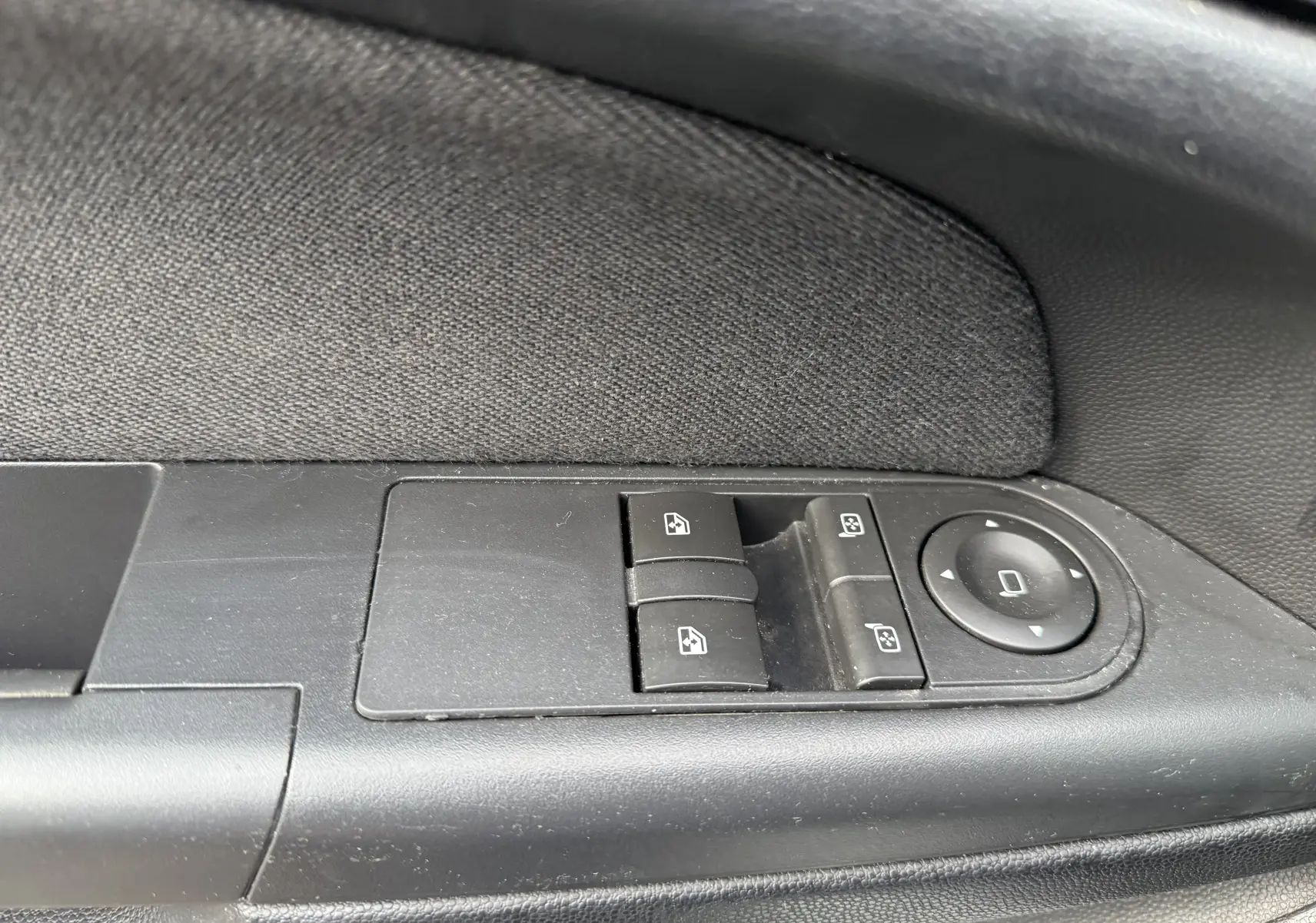 Gros plan sur les commandes électriques des vitres et rétroviseurs sur la portière côté conducteur d'une Opel Astra gris 2010.