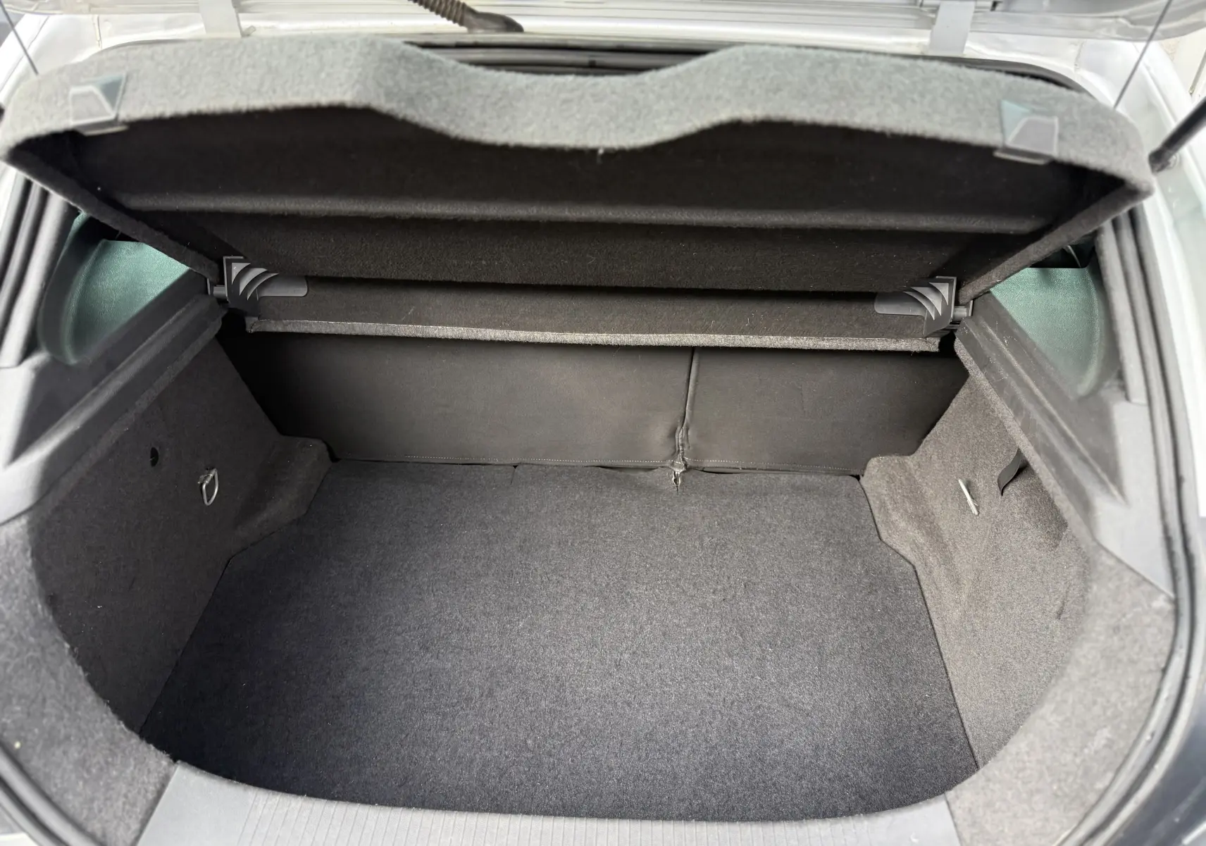 Vue intérieure du coffre ouvert d'une Opel Astra gris 2010, montrant un espace de rangement propre et vide.
