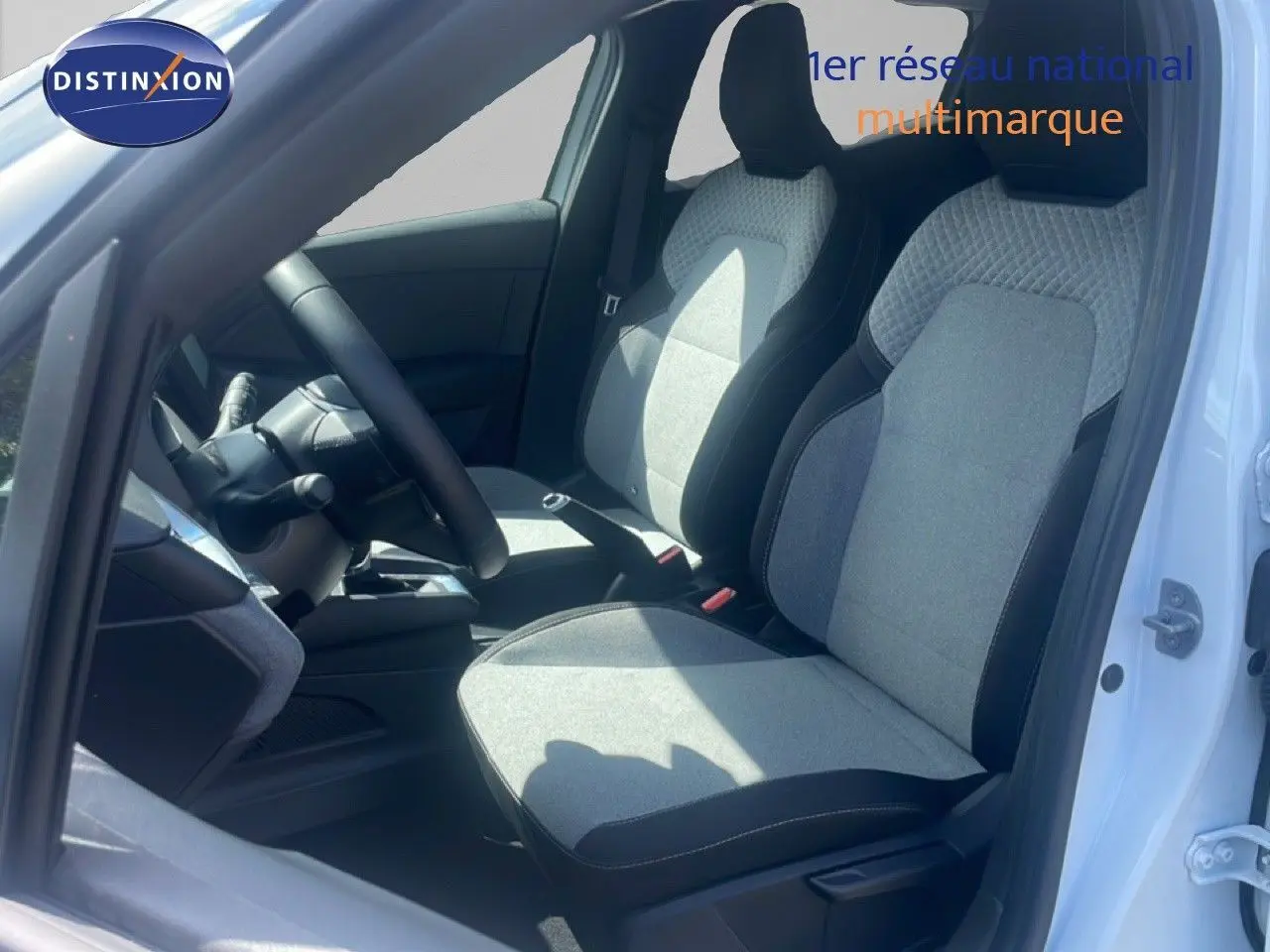 Vue intérieure côté conducteur de la Renault Clio blanche 2025, mettant en valeur les sièges tissu gris et noir.