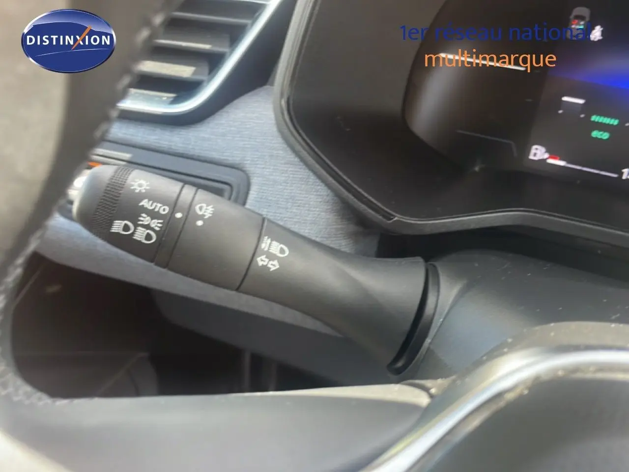 Gros plan sur la commande des feux et clignotants à gauche du volant dans l’habitacle noir de la Renault Clio blanche.