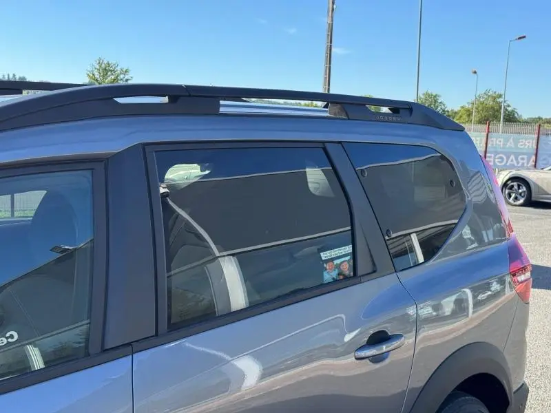 Vue latérale droite sur la partie arrière d'un Dacia Jogger gris schiste métallisé avec barres de toit et vitres teintées.