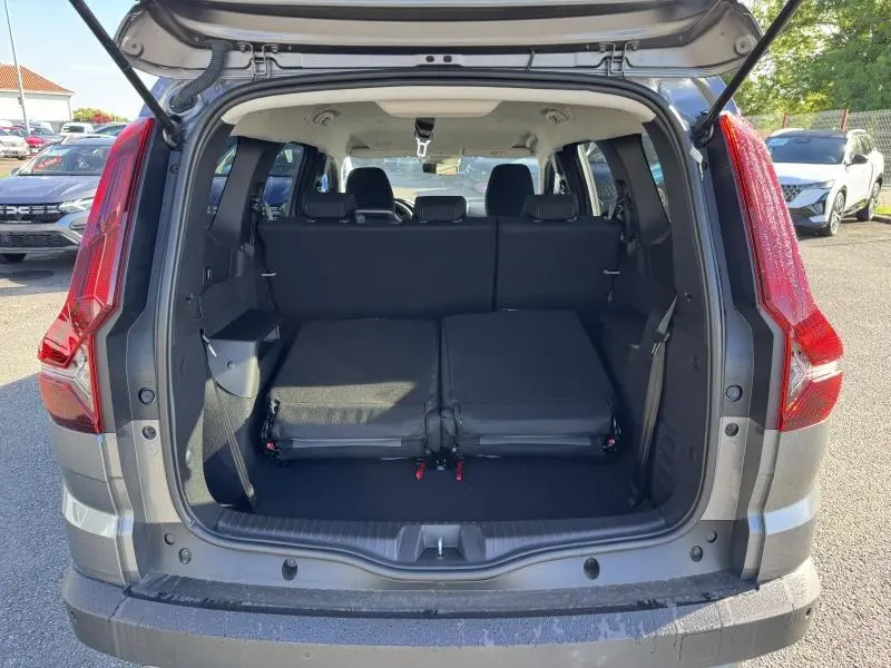 Coffre ouvert du Dacia Jogger gris schiste métallisé, montrant la banquette arrière partiellement rabattue et l'espace de chargement.