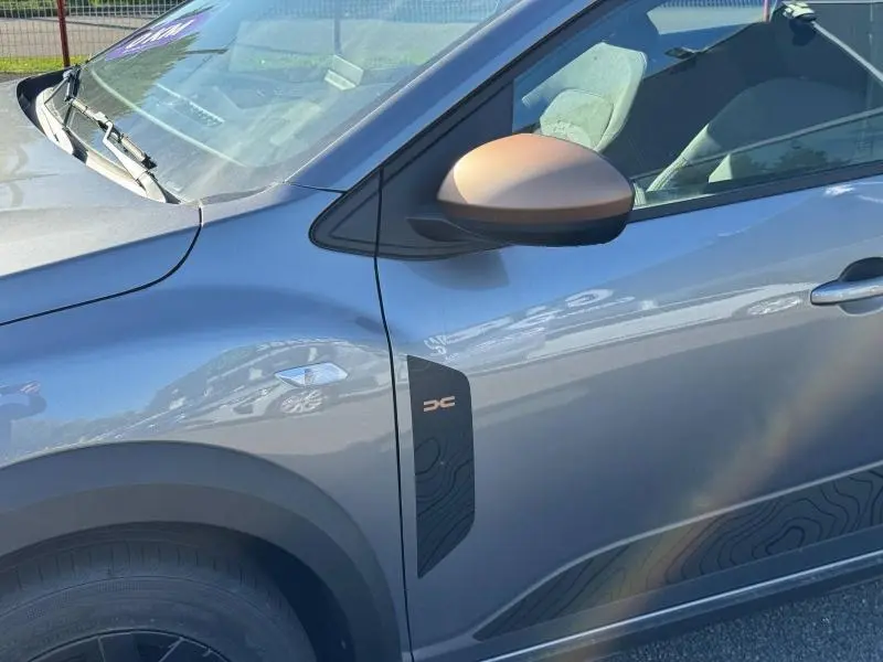 Vue rapprochée du côté gauche d’un Dacia Jogger gris schiste métallisé avec rétroviseur bronze et logo Extreme+ sur l’aile avant.