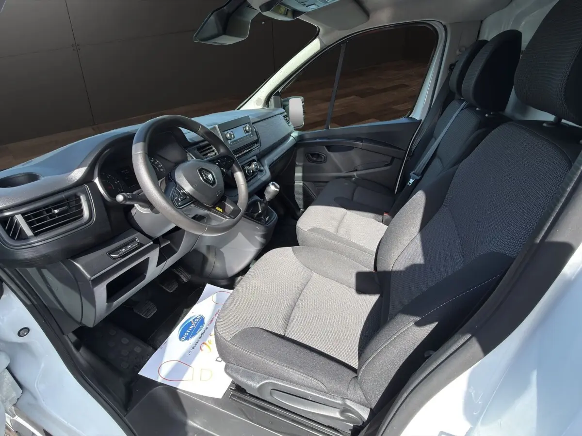 Vue intérieure côté conducteur du Renault Trafic Fourgon blanc 2024, montrant le tableau de bord et les sièges tissu gris.