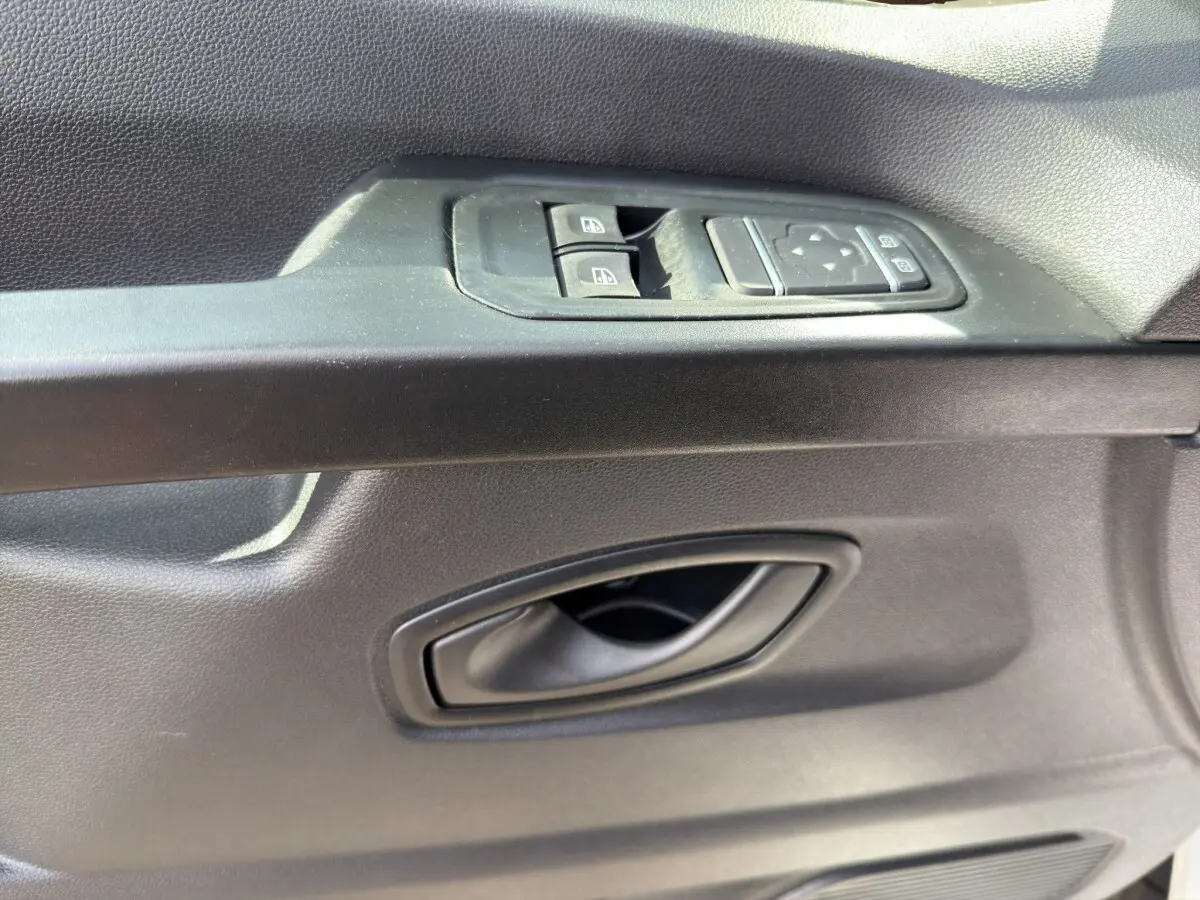 Gros plan sur la poignée intérieure et les commandes des vitres côté conducteur du Renault Trafic Fourgon blanc.