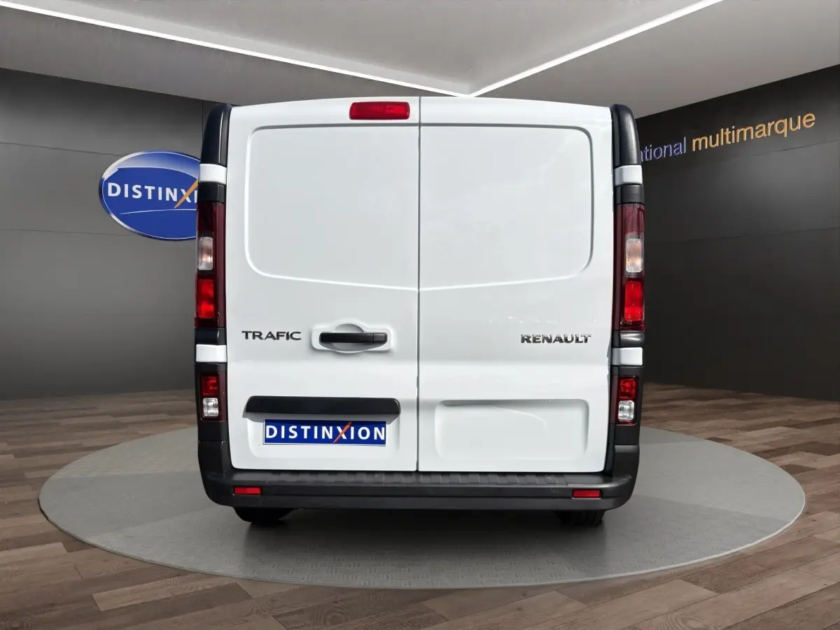 Vue arrière du fourgon blanc Renault Trafic avec portes battantes et feux verticaux rouges, en showroom.