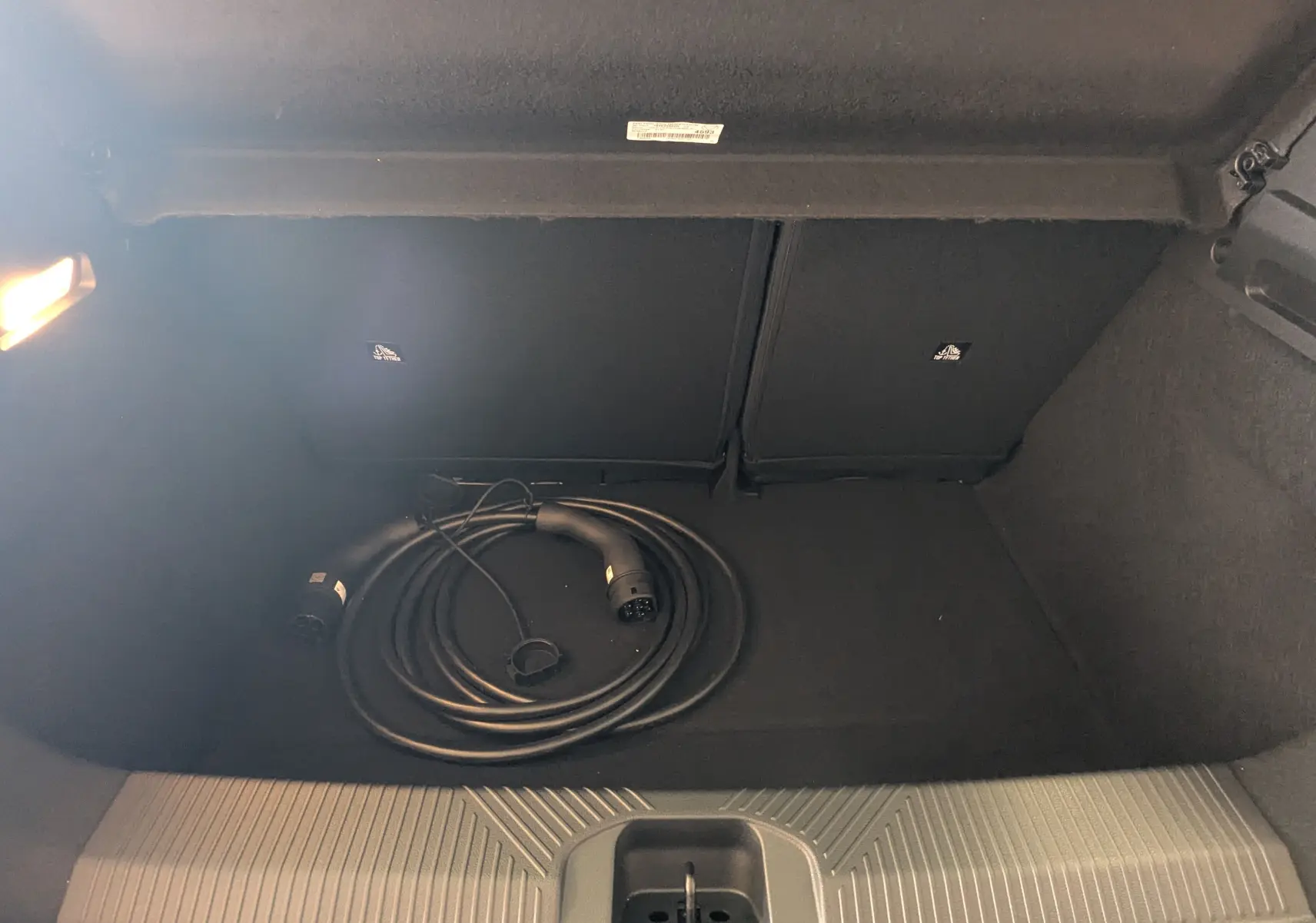 Coffre arrière ouvert de l'Alpine A290 blanc toit noir, vue plongeante sur câble de recharge électrique enroulé.