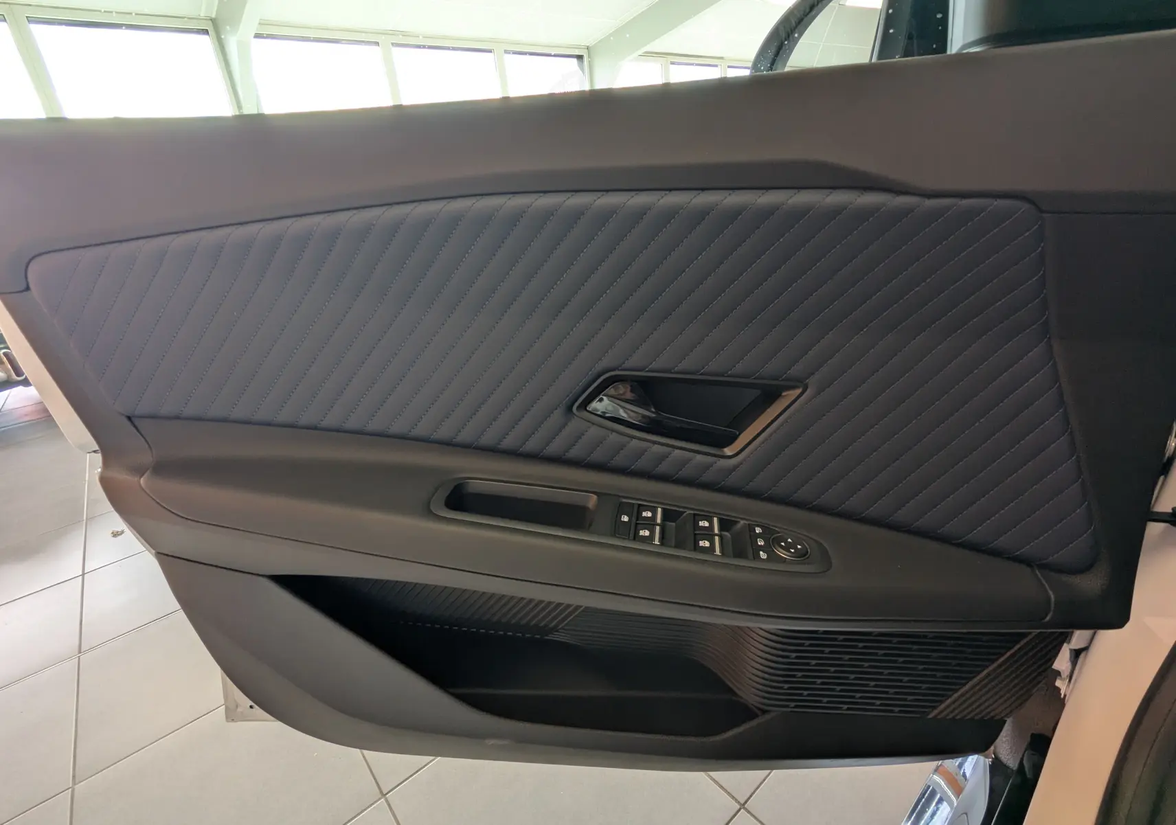 Gros plan sur la garniture intérieure de porte côté gauche de l'Alpine A290 blanc toit noir avec surpiqûres diagonales bleues.