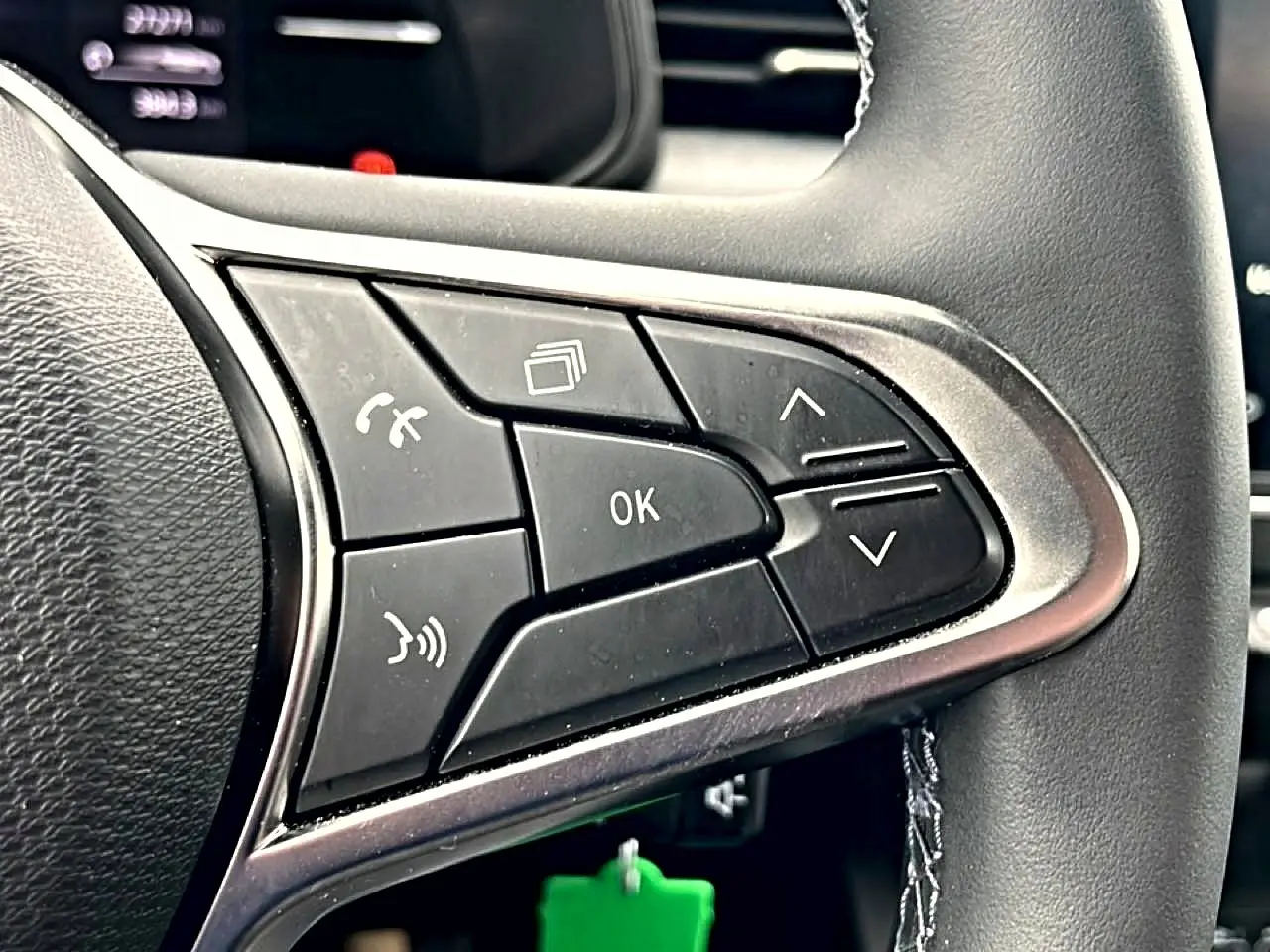 Gros plan sur les commandes multifonctions noires du volant côté gauche d’une Renault Clio V blanche.