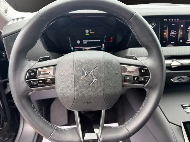 Gros plan sur le volant cuir noir multifonctions du DS4 E-TENSE 225 Cross Trocadero 2023 avec tableau de bord digital en arrière-plan.