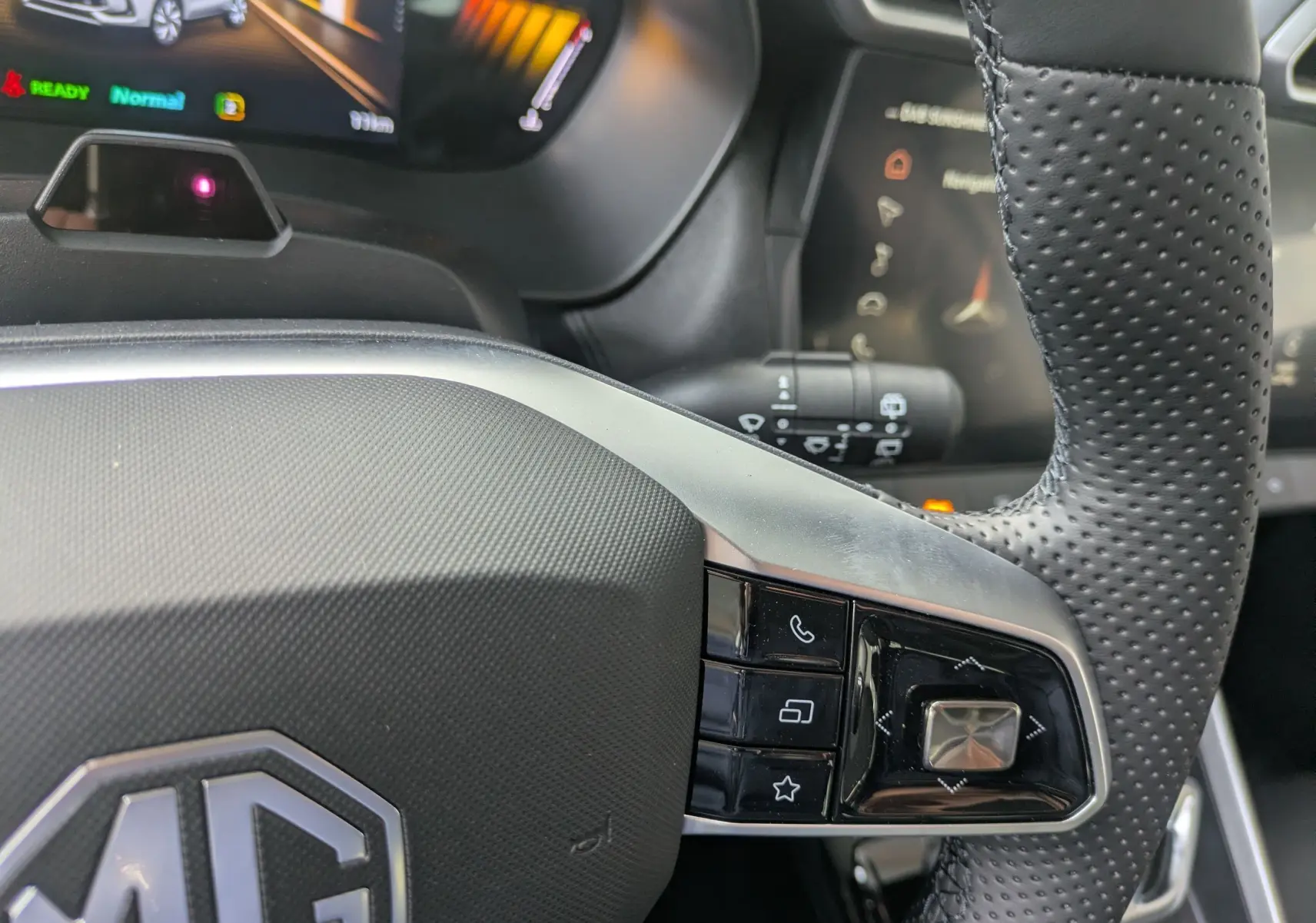 Gros plan sur le volant en cuir perforé noir du MG Motor ZS 2026, avec commandes intégrées et tableau de bord numérique en arrière-plan.