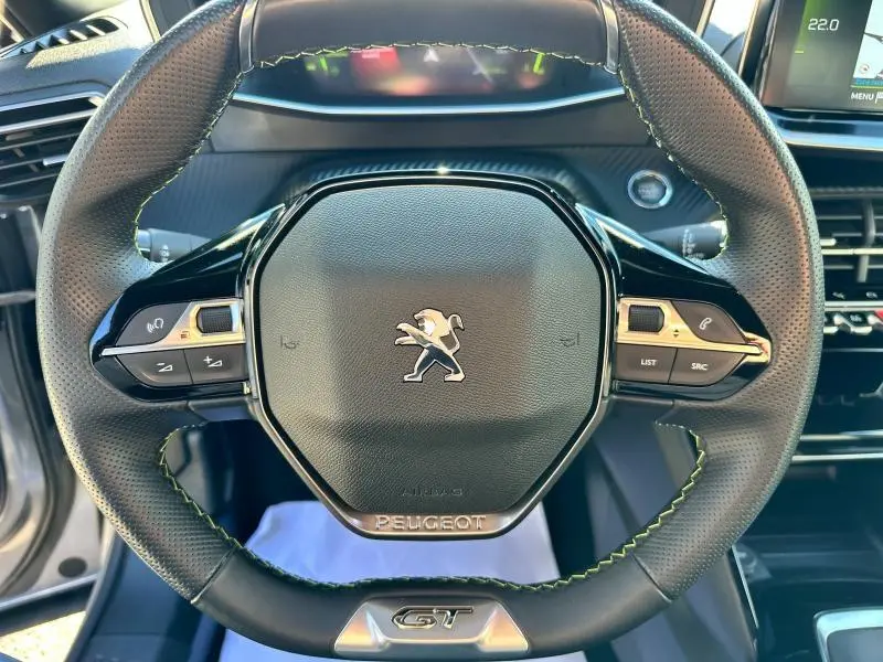 Volant cuir noir avec surpiqûres vertes du Peugeot 2008 GT, vue rapprochée centrée sur le logo et commandes intégrées.