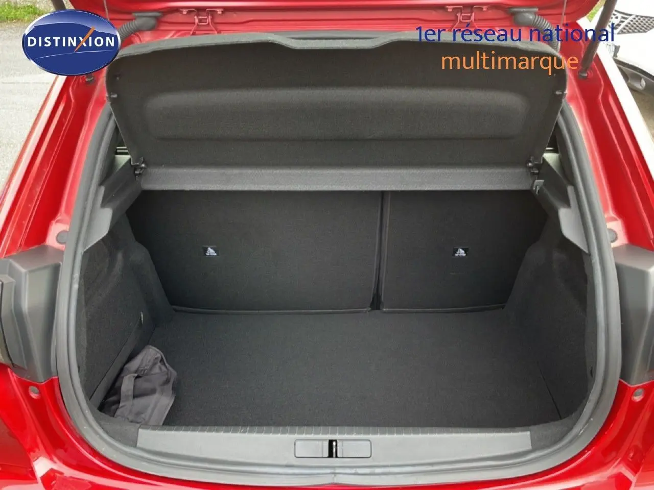 Coffre ouvert vu de l'arrière d'une Peugeot 208 rouge Elixir Metal, montrant un espace de rangement propre et vide.