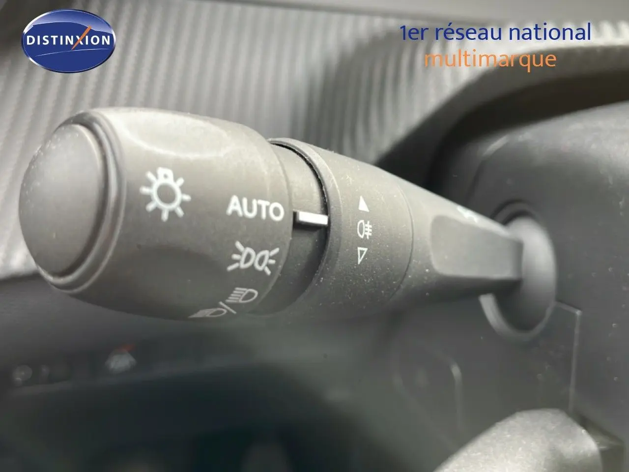 Gros plan sur la manette de commande des phares à gauche du volant dans l’habitacle d’une Peugeot 208 rouge Elixir Metal.