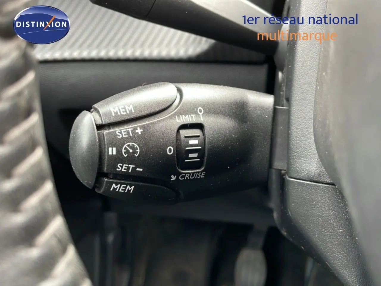 Gros plan sur la commande de régulateur de vitesse noire dans l'habitacle d'une Peugeot 208 rouge Elixir Metal.