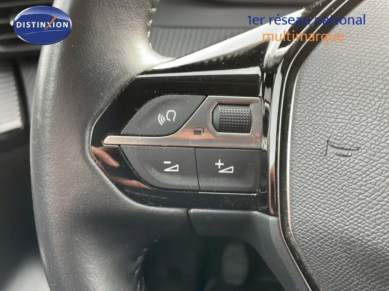 Détail du volant avec commandes audio sur la gauche d'une Peugeot 208 rouge Elixir Metal, version 2022.