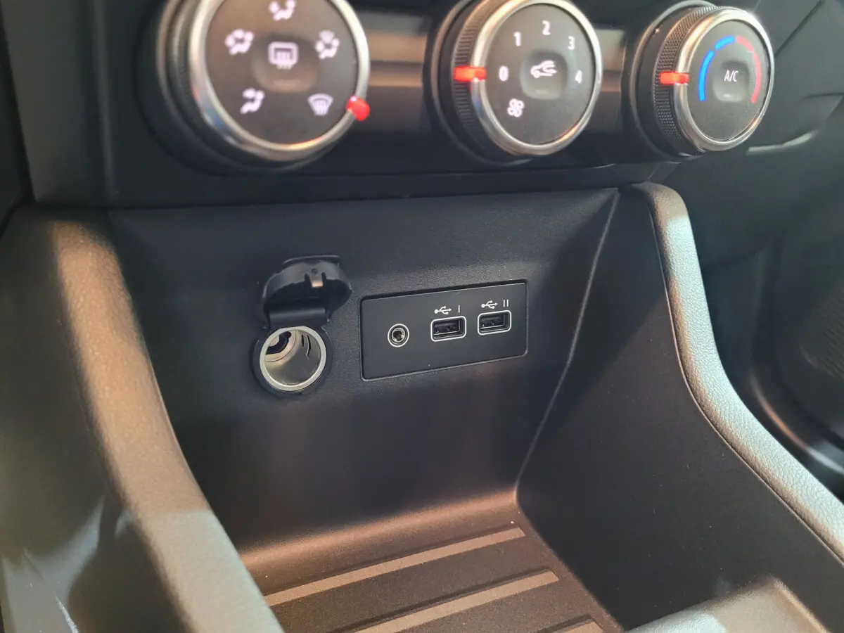 Gros plan sur la console centrale noire de la Renault Clio gris foncé, montrant prises USB et prise 12V sous les commandes de climatisation.
