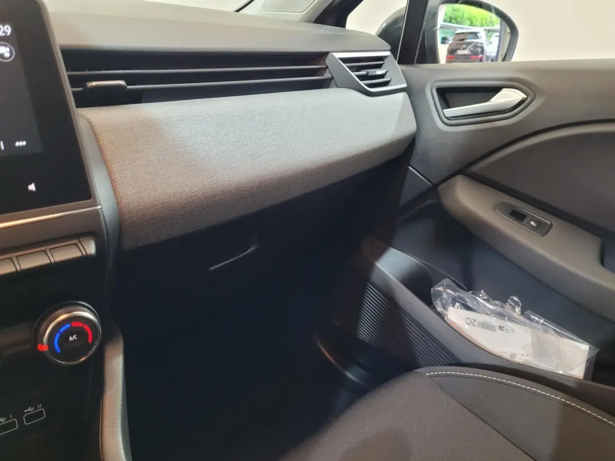 Vue intérieure côté passager de la Renault Clio gris foncé 2025, montrant la planche de bord et la portière avec commandes.