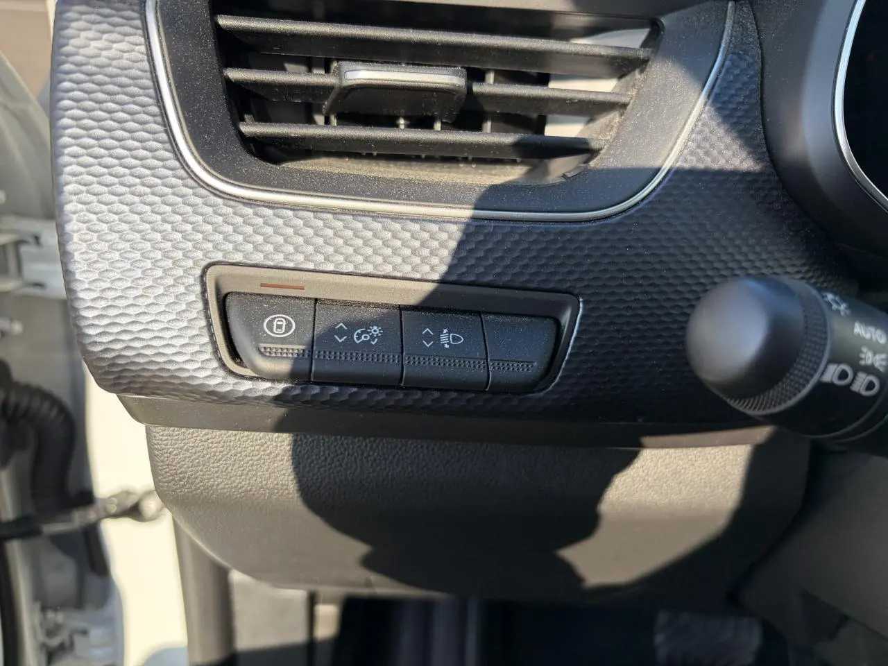 Détail du tableau de bord noir texturé avec commandes d’éclairage et ventilation du Renault Arkana blanc glacier 2025.