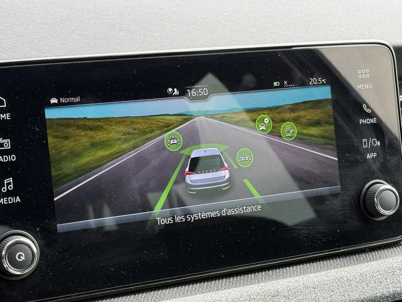 Écran tactile intérieur affichant l'aide à la conduite avec vue arrière stylisée d'une Skoda Scala blanche sur route.