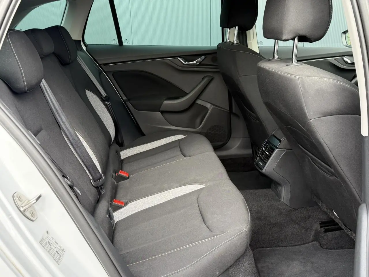 Vue intérieure arrière côté gauche de la Skoda Scala TSI 116 DSG7 blanche, sièges tissu gris avec surpiqûres claires.