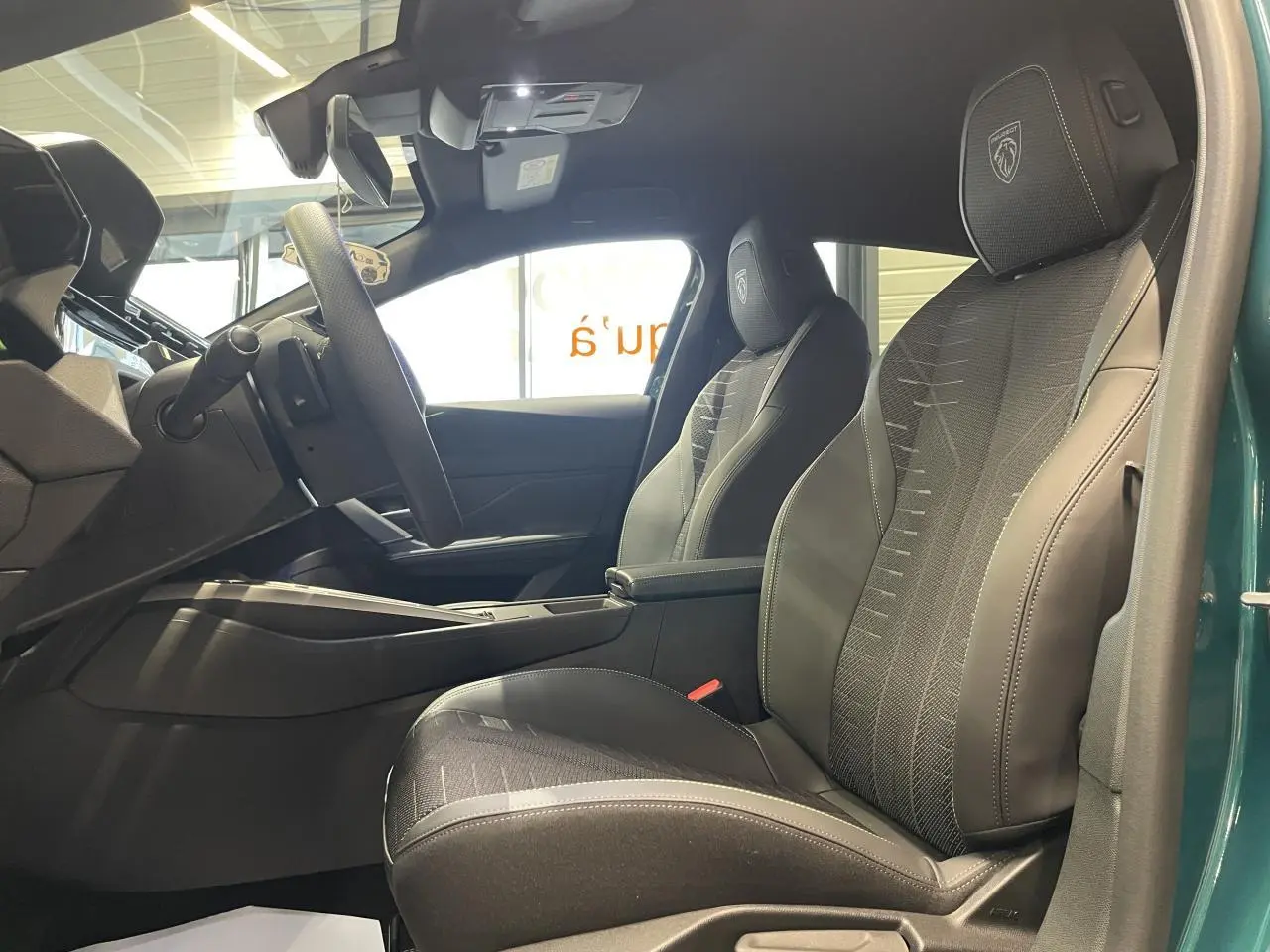 Vue intérieure côté droit de la Peugeot 308 2026, sièges tissu noir avec surpiqûres et logo Peugeot brodé.