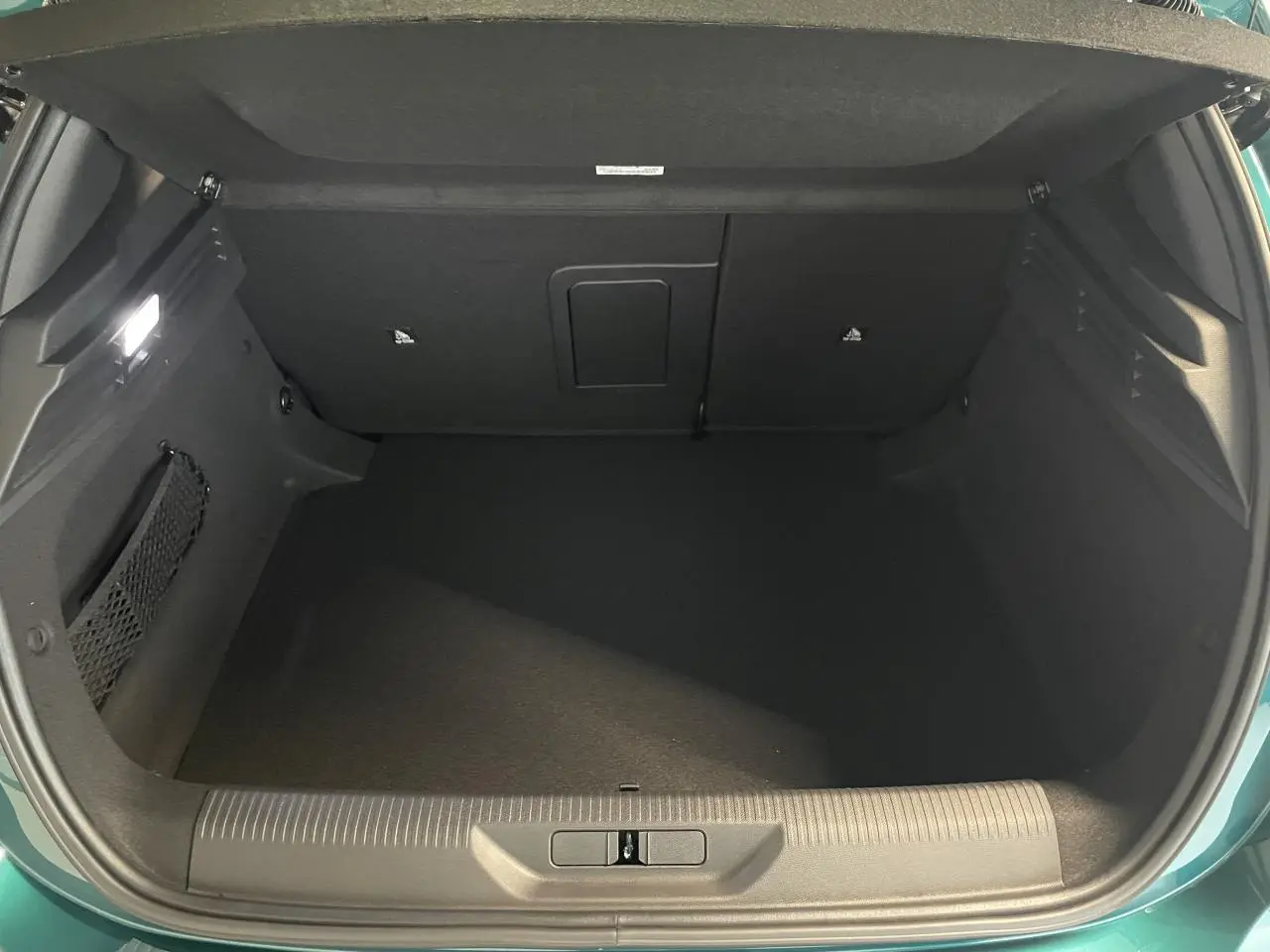 Coffre ouvert de la Peugeot 308 Bleu Lagoa, vue arrière montrant l'espace de rangement vide et l'éclairage intérieur.