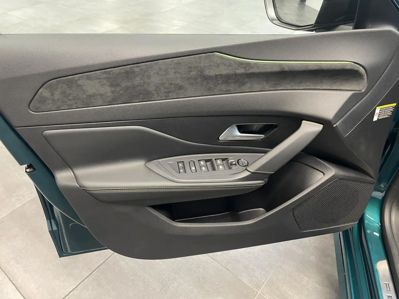 Vue intérieure côté gauche de la porte avant bleu métallisé avec garniture noire et surpiqûres vert Adamite sur Peugeot 308 2026.