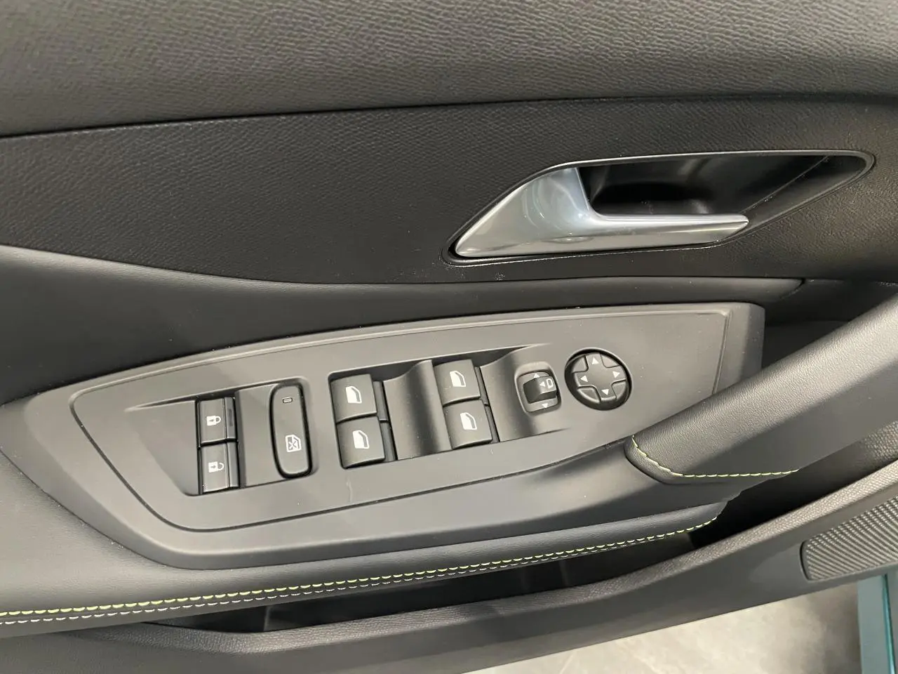 Gros plan sur la commande des vitres et rétroviseurs côté conducteur de la Peugeot 308 GT bleu avec surpiqûres vert Adamite.
